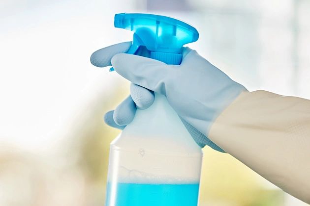 Hand in glove dispensing blue liquid sanitizer from pump bottle