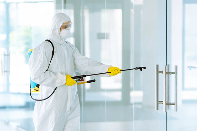 Professional in protective suit disinfecting modern office space with spray equipment.