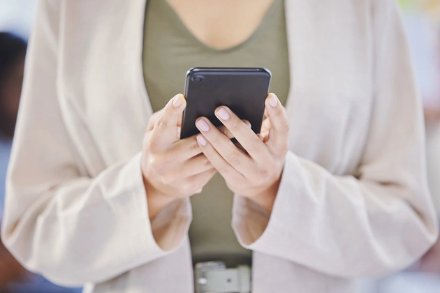 Person in white cardigan holding smartphone, dental practice setting.