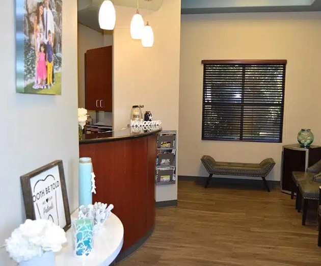 Modern dental office reception area with wooden furniture, pendant lighting, and comfortable seating.