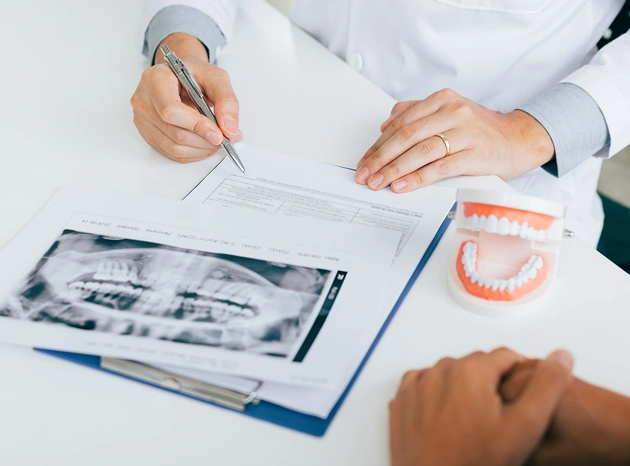 Dentist reviewing X-rays and dental model with patient at consultation desk