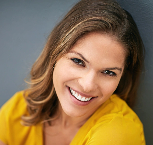 Smiling woman in yellow shirt against gray background, professional headshot for dental practice.