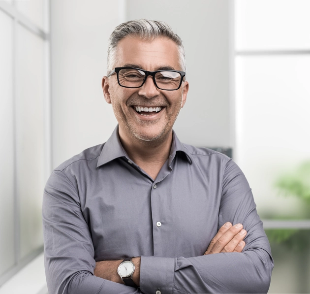 Professional man with glasses smiling, arms crossed, in bright modern dental office setting.