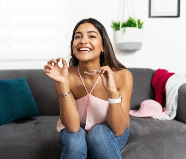 Happy woman sitting on couch, holding dental floss, promoting oral hygiene care.