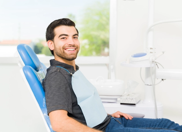 Young man sitting in blue dental chair smiling at modern dental office