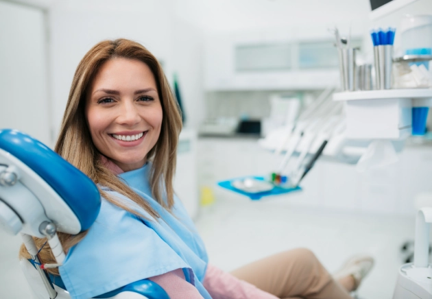 Female dental professional in blue scrubs smiling in modern dental office setting.