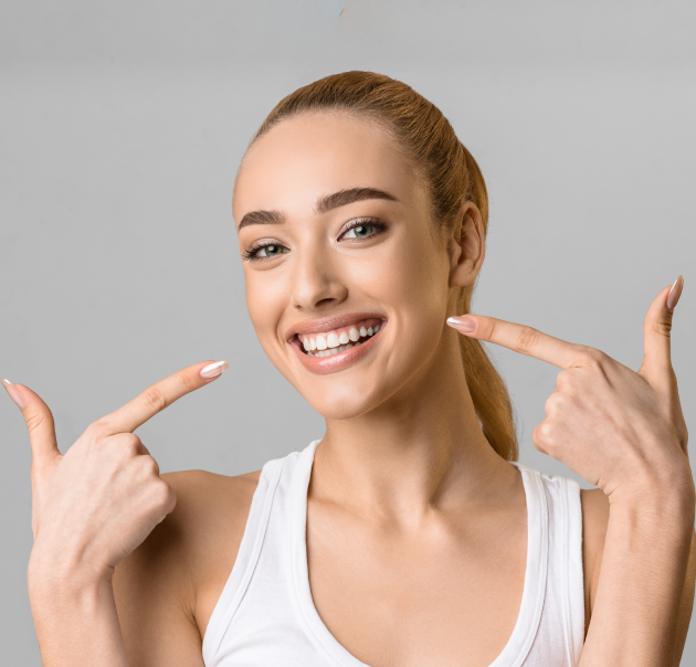 Smiling woman pointing to her teeth against gray background, dental health portrait.