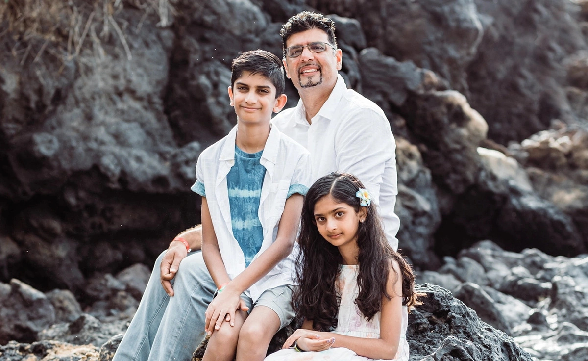 Family of three posing together outdoors on rocky terrain with evergreen trees in background.