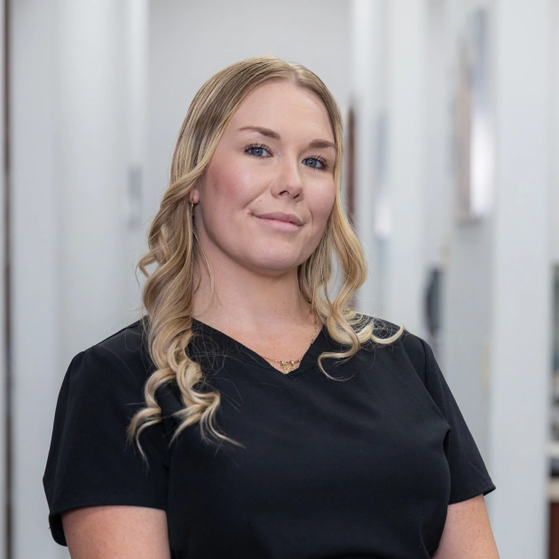 Professional woman in black shirt smiling at dental office, indoor clinical setting.