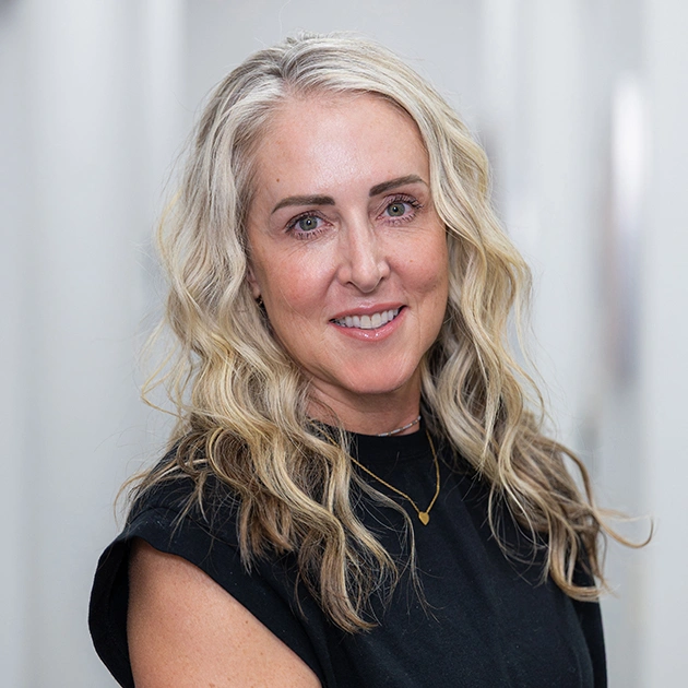 Professional headshot of blonde woman smiling at camera in modern dental office setting.