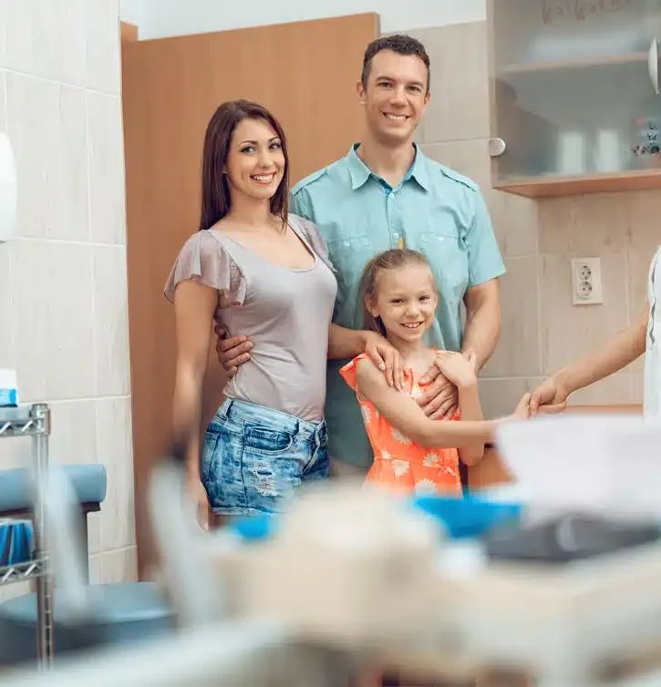 Family of three in a bright dental office bathroom, smiling together near sink and mirror.