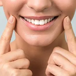 Person smiling brightly while pointing to their teeth against neutral background