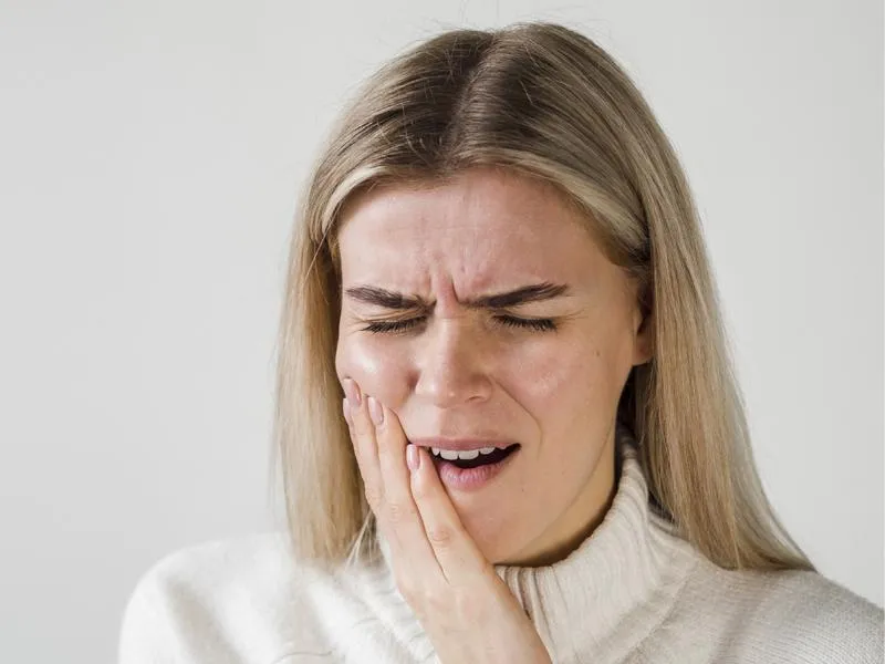 Woman experiencing tooth pain, holding cheek, white background, dental concern expression.