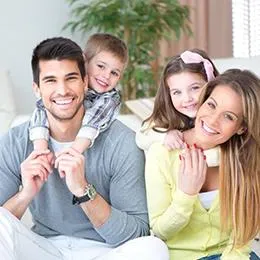 Happy family of four smiling together indoors in bright, casual setting.
