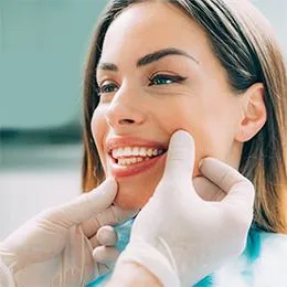 Smiling woman receiving dental examination with gloved dentist's hands near her mouth at beach.