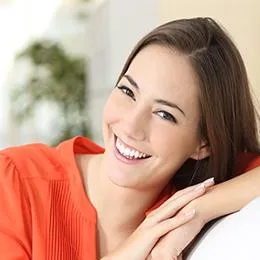 Woman in orange shirt smiling at camera in bright dental office setting