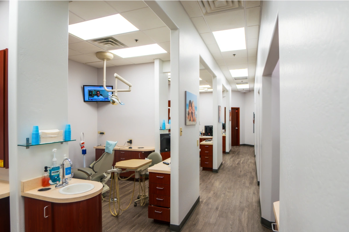 Modern dental office reception and treatment area with white walls, clinical equipment, and wooden cabinetry.