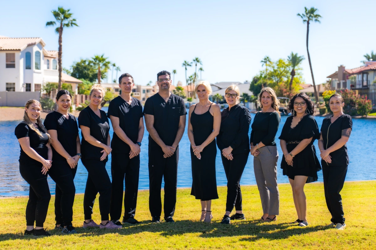 Island Dental team standing together on sunny grass with palm trees and waterfront in background.