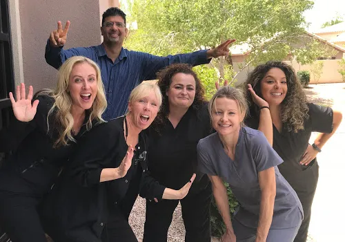 Dental team members waving at camera outdoors in casual group photo.