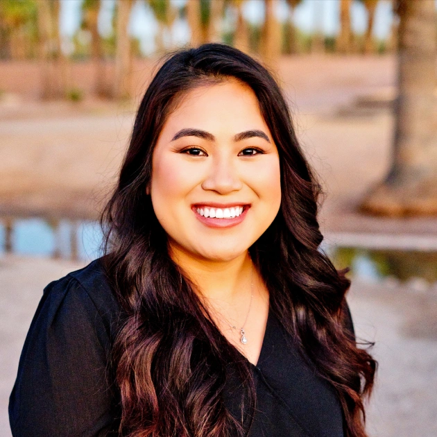 Professional woman smiling at camera in black blazer, indoor dental office setting.