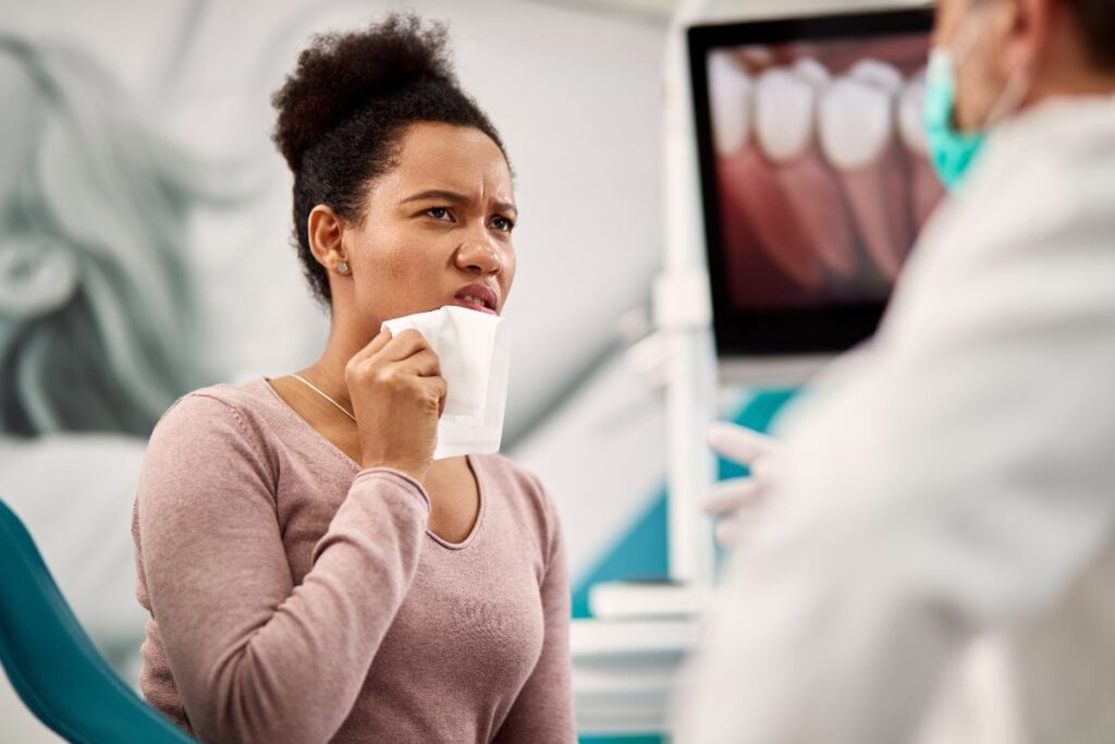 A patient speaks with a dentist while holding her jaw in discomfort, representing the professional evaluation process used to diagnose cracked teeth.