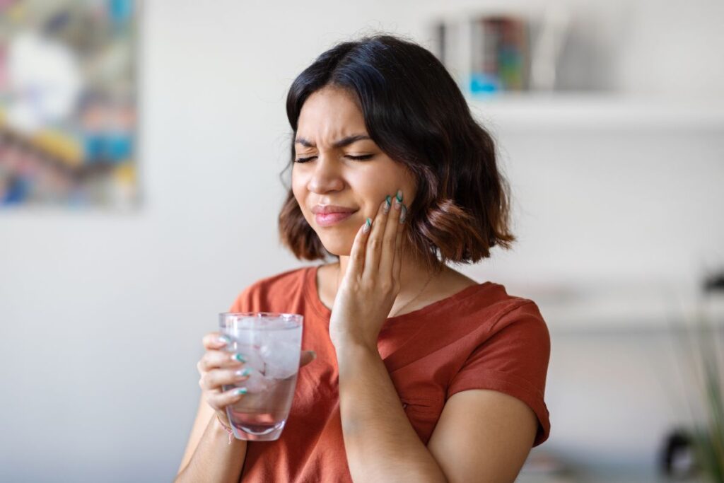 A woman reacts to tooth discomfort while holding a cold drink, illustrating sudden tooth sensitivity to hot or cold foods and beverages.
