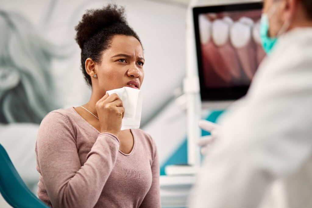 A woman experiencing tooth pain holds a tissue to her cheek while discussing her dental concerns with a dentist in the clinic.