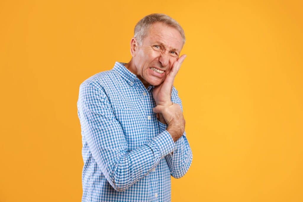 A man experiencing severe tooth pain holds his cheek, illustrating worsening discomfort several days after a dental procedure that may require immediate evaluation by a dentist.