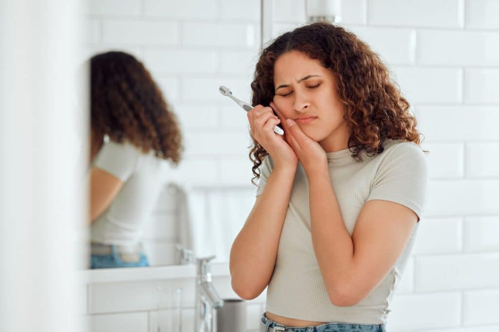A person experiencing persistent tooth pain holds their cheek while holding a toothbrush, illustrating a common sign that it's time to schedule a dental examination.