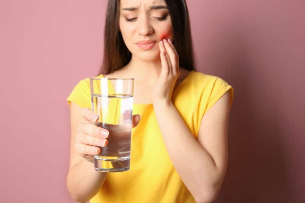 Woman experiencing tooth sensitivity while drinking water after a cavity, highlighting the importance of early Dental Fillings Gilbert treatment.
