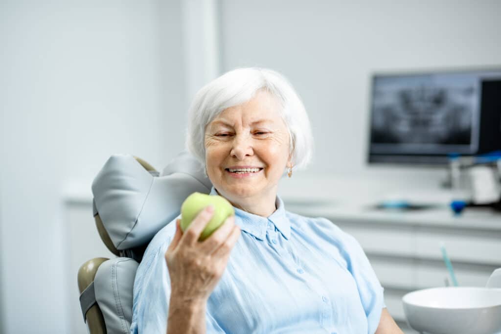 Adult eating a raw apple while adjusting to new dentures